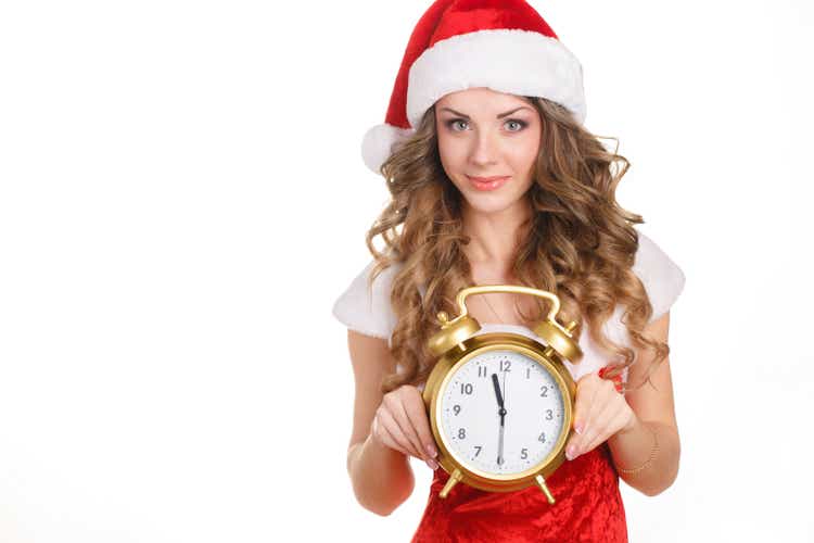 Young beautiful woman in Santa hat holding big clock on white background. Christmas celebration.