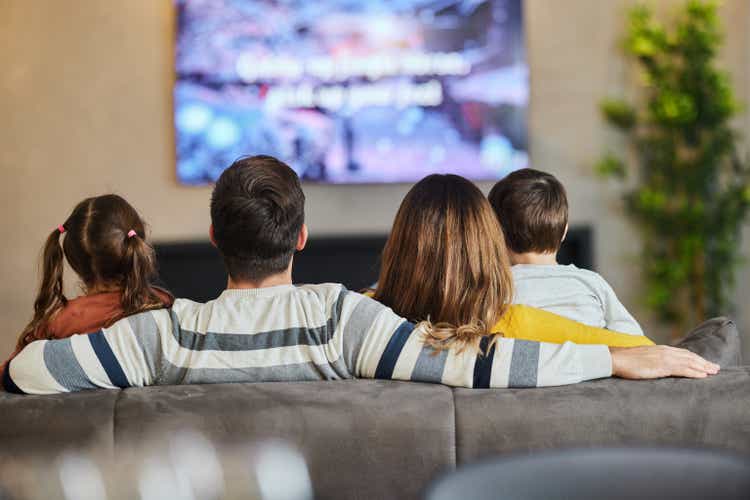 Back view of a family watching TV at home.