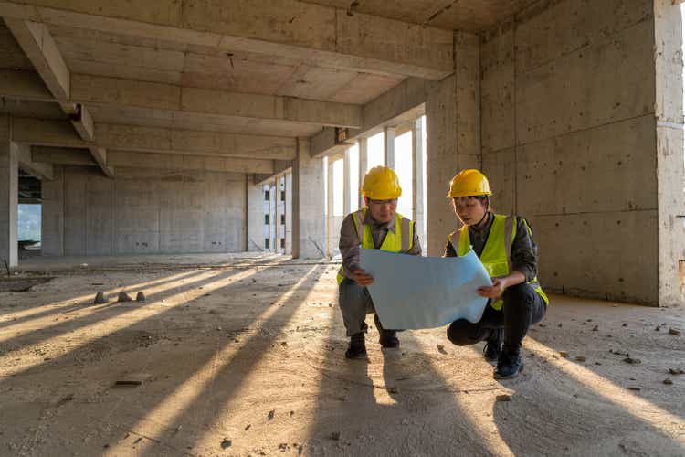 Ingenieros de construcción masculinos y femeninos con dibujos que comparan datos