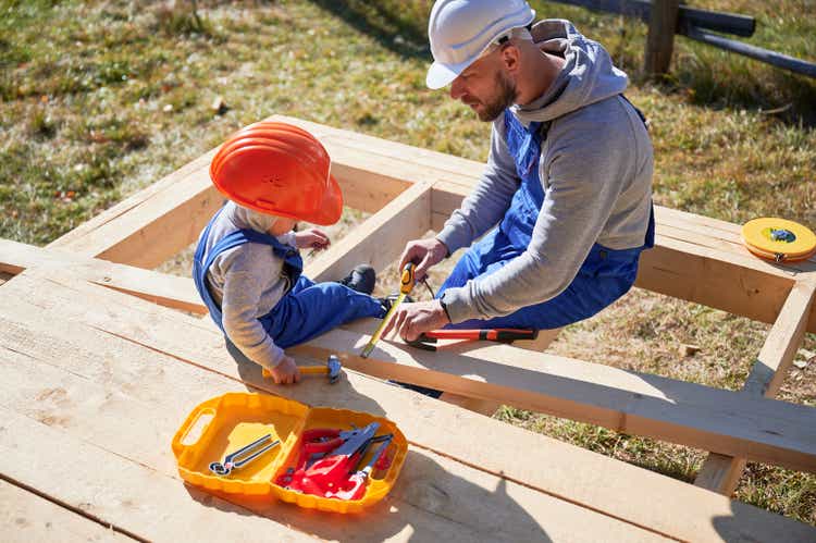 Father with toddler son building wooden frame house.
