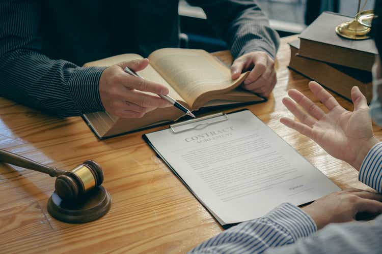 Il consulente legale presenta un contratto firmato con il Martello e la Bilancia della Dea della Giustizia su un tavolo o in una riunione di squadra in ufficio.