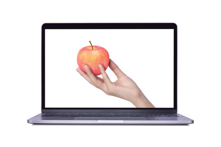 Hand hold pink fuji apple on laptop computer screen isolated on white background.