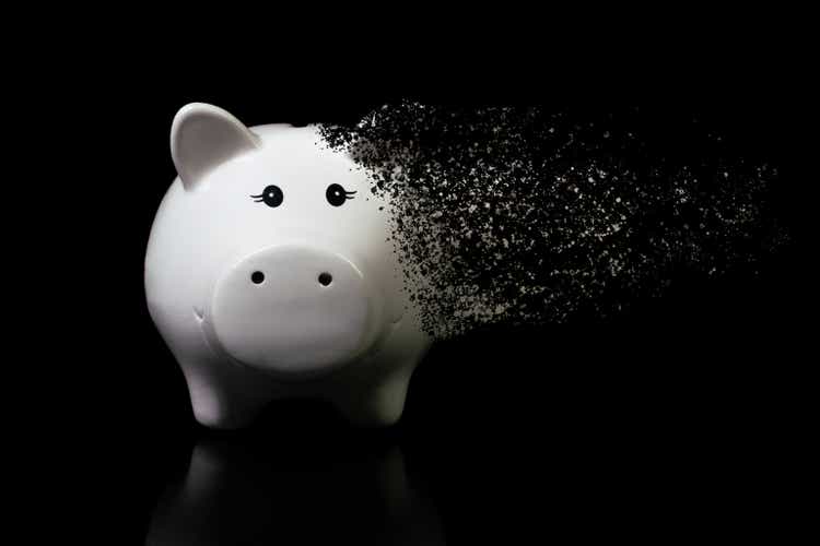 White piggy bank dispersed on a very dark surface. Concept for economic crisis, inflation, devaluation, financial loss, devalued savings, market problems.