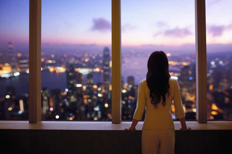 Young woman in suit looks at Hong Kong skyline from window in building