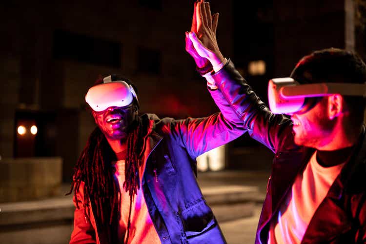 Young multiracial friends playing in virtual reality and win, people giving five to eac other with ar googles, neon light effect, nft transaction success, focus on hands