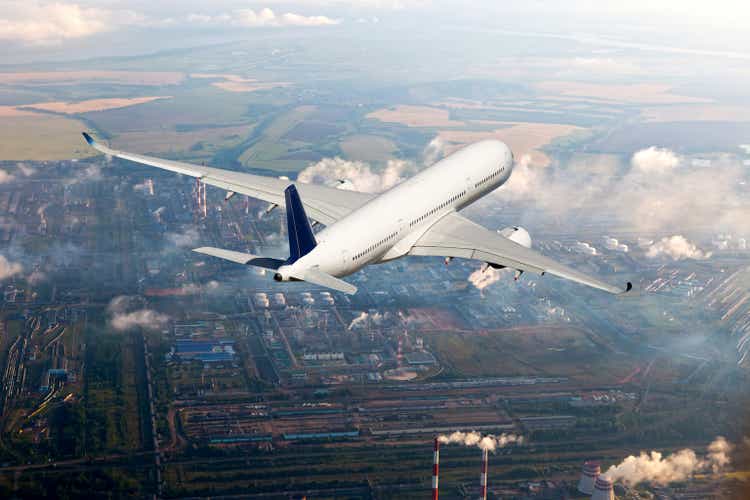 White passenger plane flies high above the big city. Back view of aircraft.