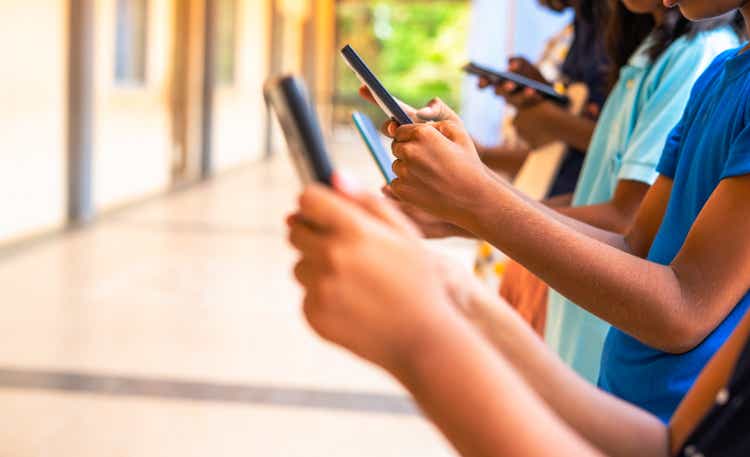 Close up shot, group of children hands busy using smartphone at school corridor - concept of social media, playing games, technology and education