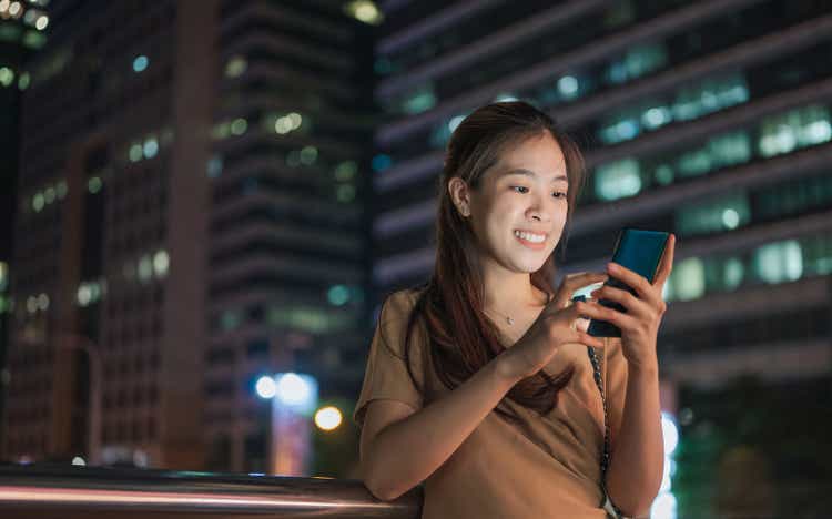 Young asian on public transportation platform using mobile investing ETF and fund bond saving at Central business distric