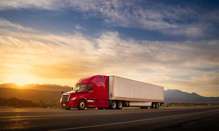 Red and white semi truck speeding at sunrise on a single lane road USA