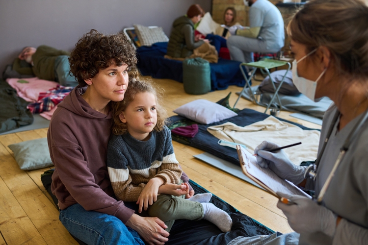 Young female refugee with son looking at clinician making notes in document