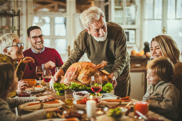 Happy senior man serving Thanksgiving turkey for his family at dining table.