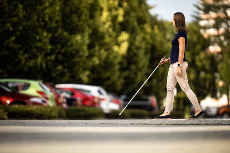 Blind woman walking on city streets, using her white cane