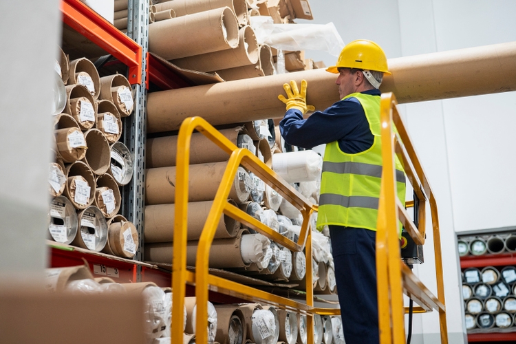 Male manufacturing plant worker pulling out cardboard tube from shelves
