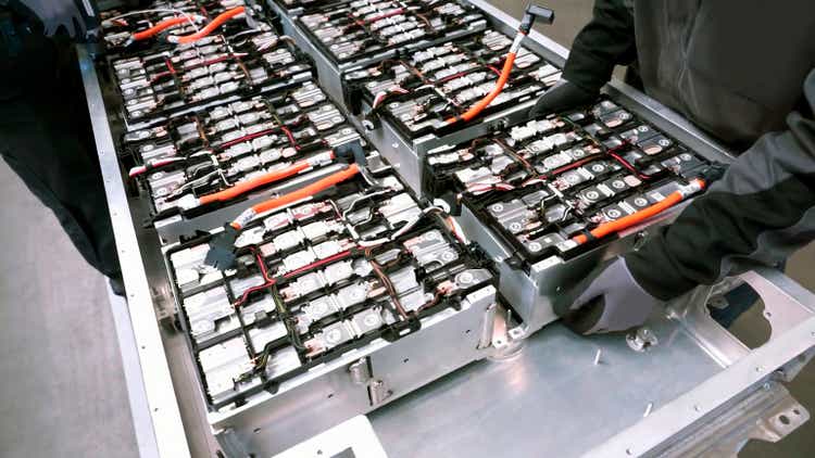 Close-up of two mechanics repairing the battery of an electric car in a car workshop.