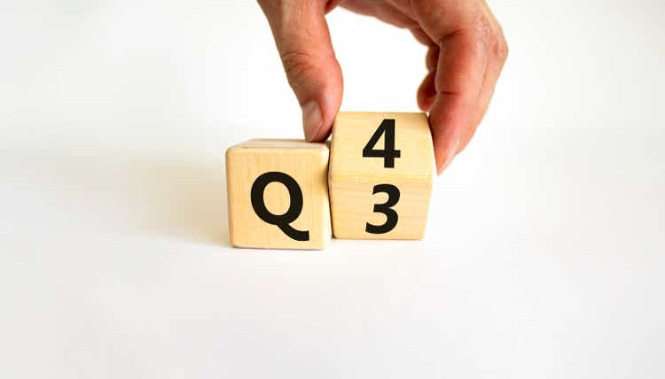 From 3rd to 4th quarter symbol. Businessman turns a wooden cube and changes words "Q3" to "Q4". Beautiful white table, white background. Business, happy 4th quarter Q4 concept, copy space.