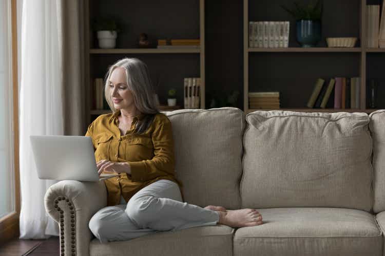 Happy senior laptop user woman sitting on couch at home