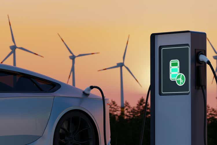 Environmentally friendly electric car charging on background of wind turbines. Evening sunset view of EV station with port plugged in car. Realistic 3d Rendering of Alternative Energy concept.