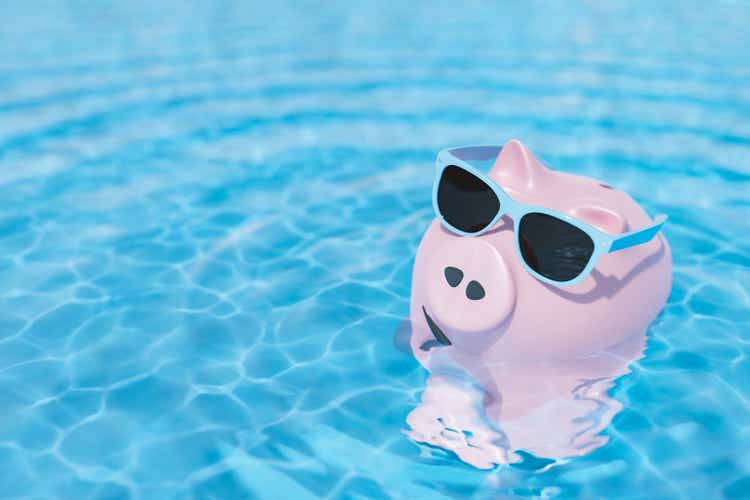 Piggy bank with sunglasses swimming in pool