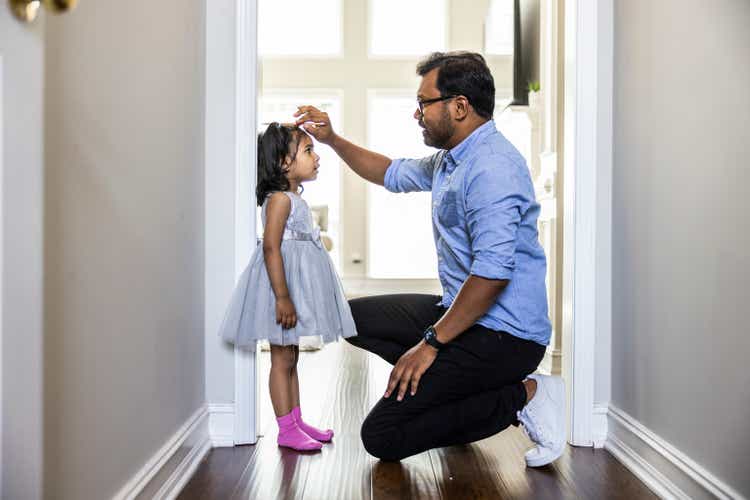 Father measuring toddlers daughter"s height against wall at home