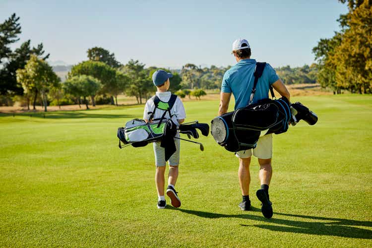 Golfer and son with golf bags walking on field