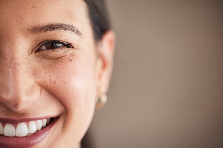 Face of beautiful mixed race woman smiling with white teeth. Portrait of a woman"s face with brown eyes and freckles posing with copy-space. Dental health and oral hygiene