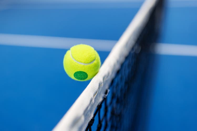 Yellow tennis ball hitting the net of blue tennis court