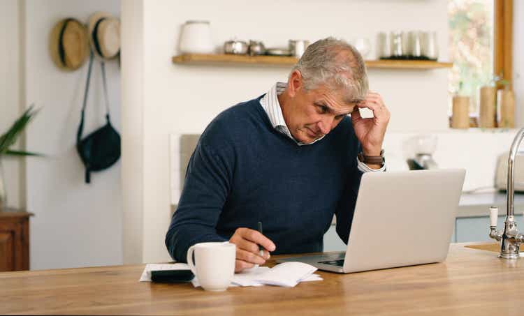 Senior man planning money, paying bills and looking frustrated while using laptop at home.Confused, stressed and unsure mature man doing paperwork and working online with computer