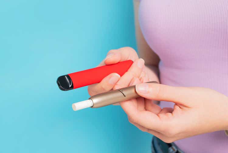 Disposable electronic cigarette and iqos in hand close up.