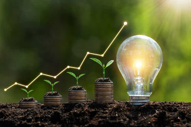 Die Glühbirne befindet sich auf dem Boden. und Pflanzen wachsen auf gestapelten Münzen Erneuerbare Energieerzeugung ist für die Zukunft unerlässlich und auf erneuerbaren Energien basierende grüne Unternehmen können Geschäftswachstum ermöglichen.