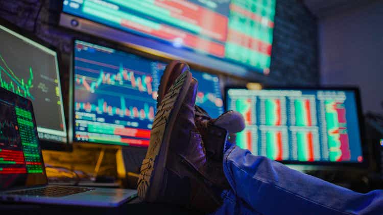 Man relaxing with feet on table in front of stock market graphs on computer screens