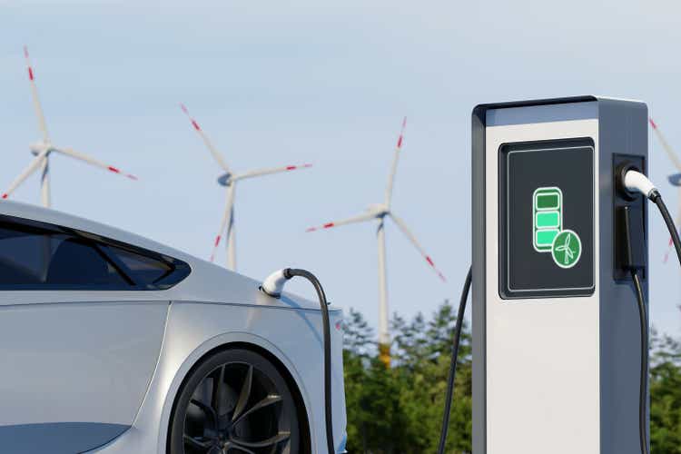 Environmentally friendly electric car charging on background of windmills. Sunny day view of EV station with port plugged in vehicle. Realistic 3d Rendering of renewable energy concept