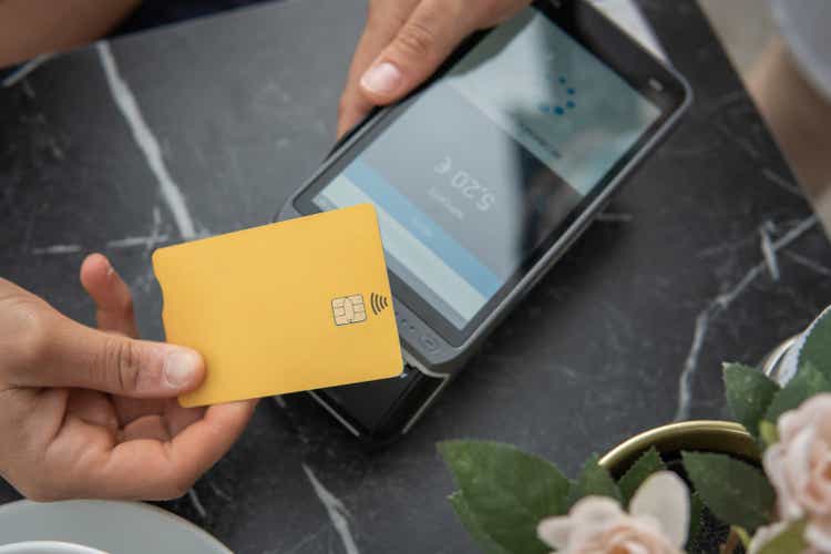 Hand holding yellow credit card to make digital payment by dataphone.