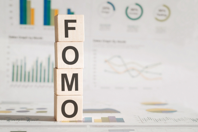 Four wooden cubes with letters FOMO meaning Fear of Missing Out on white working board.