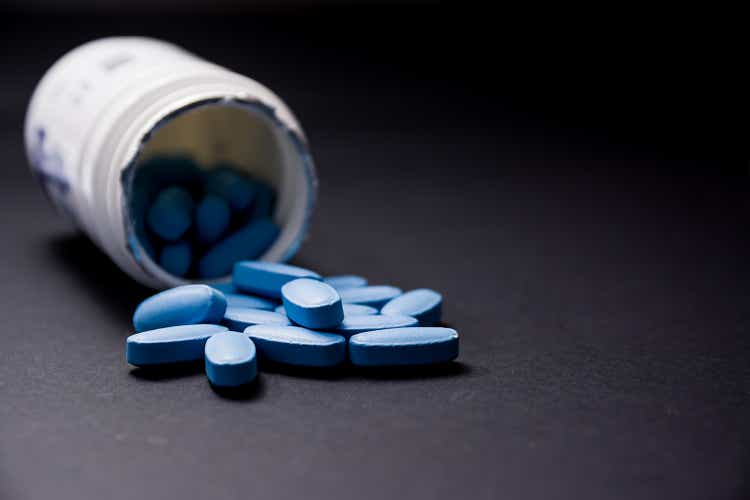 Blue pills in the foreground come out of a white plastic container on a blurred background