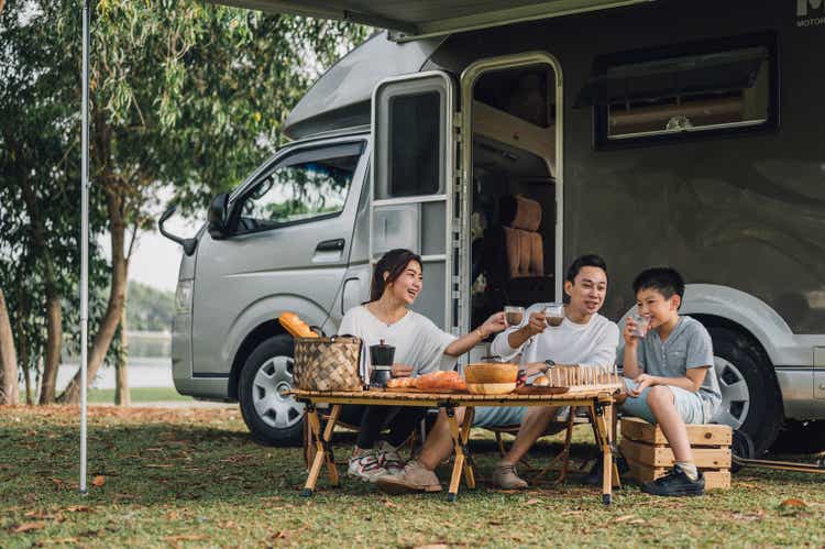 Happy Asian family talking at picnic table by the camper trailer in nature