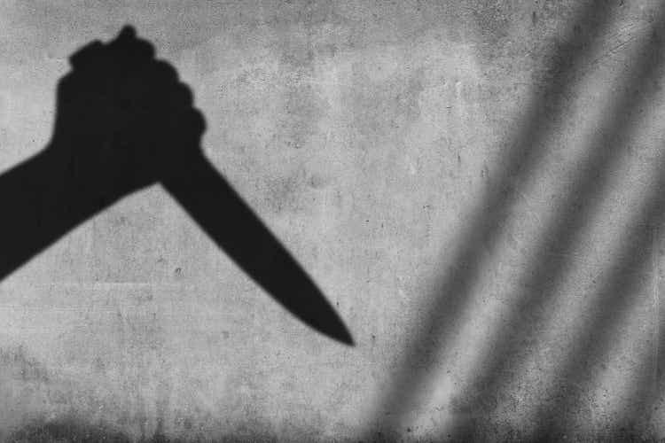 Shadow of the hand holding a knife on wall background