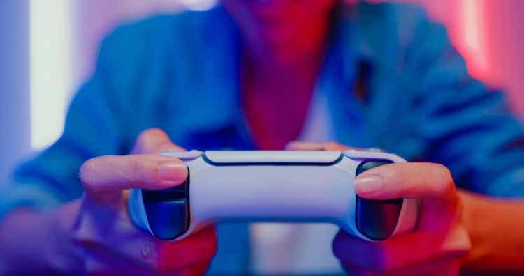 Close up of young Asian woman playing video game console in neon lights living room at home.