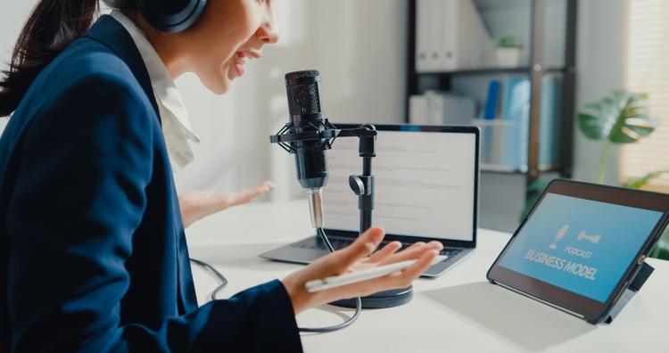 Close up of young Asian businesswoman recording and broadcasting a podcast on her laptop from studio office.