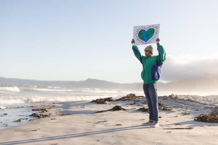 Lone teenager holding up an eco awareness placard on a windswept beach