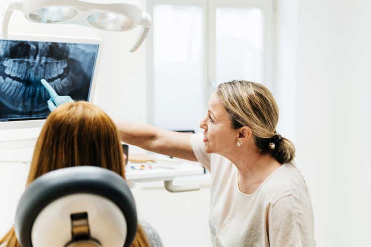 Orthodontist Pointing At Teeth On X-Ray Displayed On Surgery Monitor