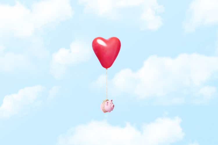 Piggy bank tied to a red heart balloon in the clouds