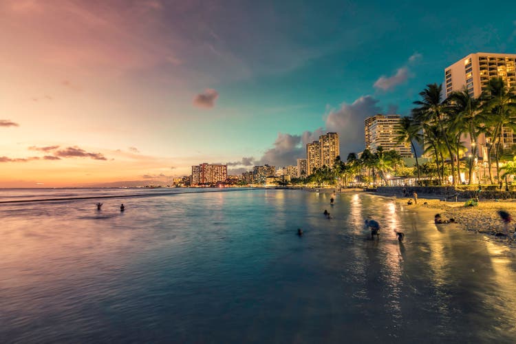 Night panorama of Waikiki Beach and building by the shore line with palm trees in Honolulu