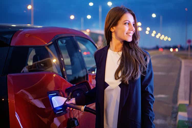 Portrait of young woman charging her electric car