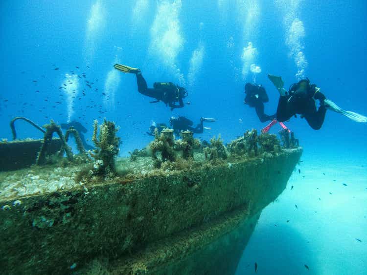 Scuba divers exploring huge ship wreck on the sea bottom