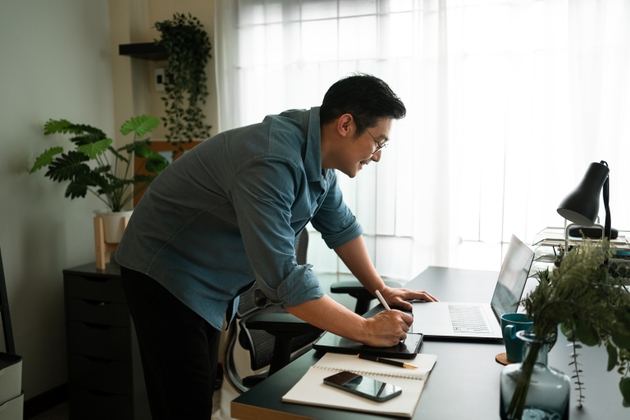 Happy man writing on digital tablet while Virtual meeting with partner on laptop computer at home. Virtual work concepts