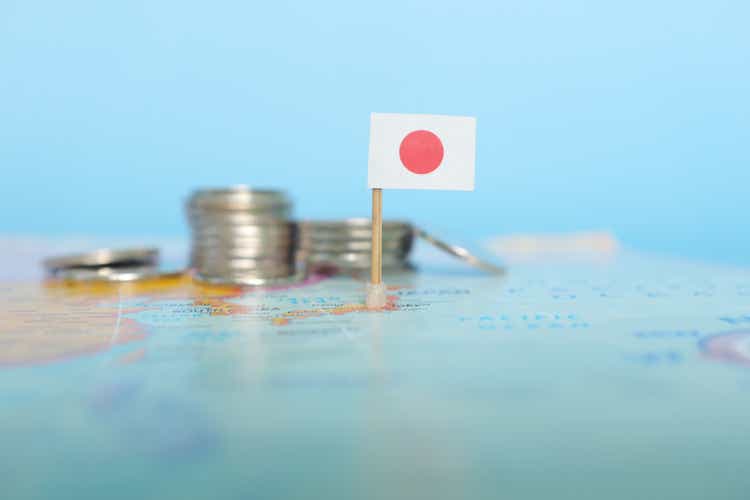 コインでぼやけた世界地図上の日本の国旗の選択的な焦点。 日本経済と富の概念。