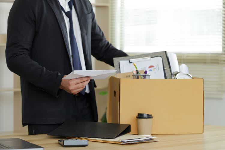 Resignation. The businessman puts his box of his belongs on the desk and holds the white letter. Quitting a job, a businessman fired or leave a job concept. The great Resignation.