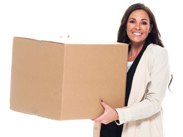 Caucasian female manager standing in front of white background wearing businesswear and holding cardboard
