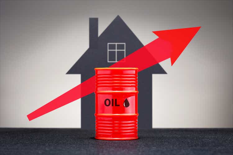 Growing oil prices concept. Barrel with heating fuel on the background of house.