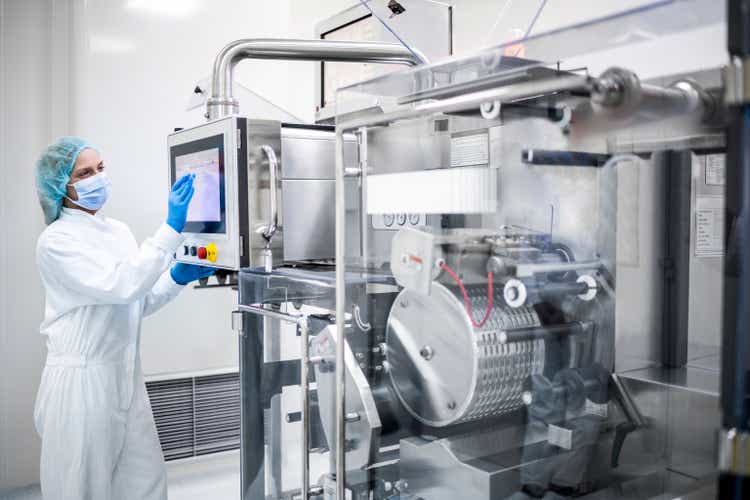 Drug manufacturing in pharmaceutical industry and its female employee seen taping on the screen of a machine
